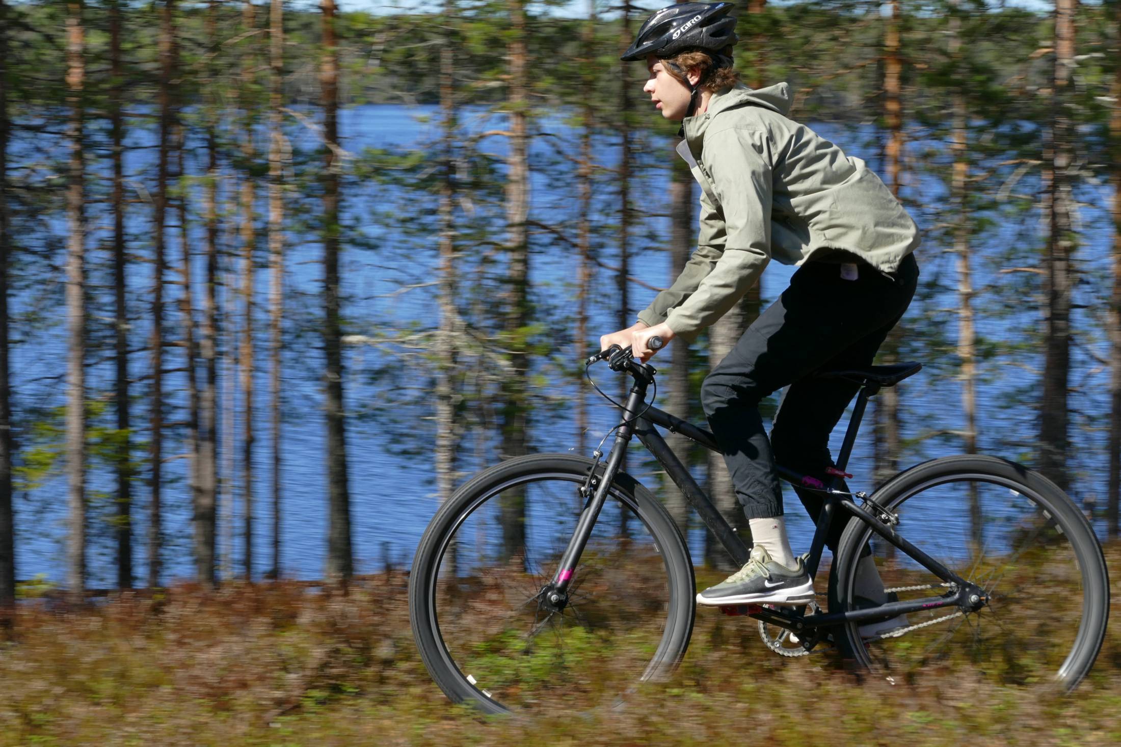Nuori pyöräilee järven rannan metsäpolulla